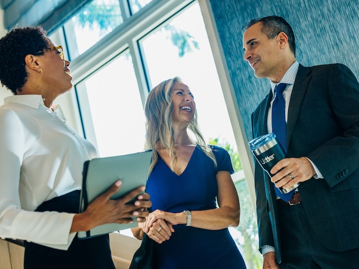 Two women talking to a man in a suit inside an office building