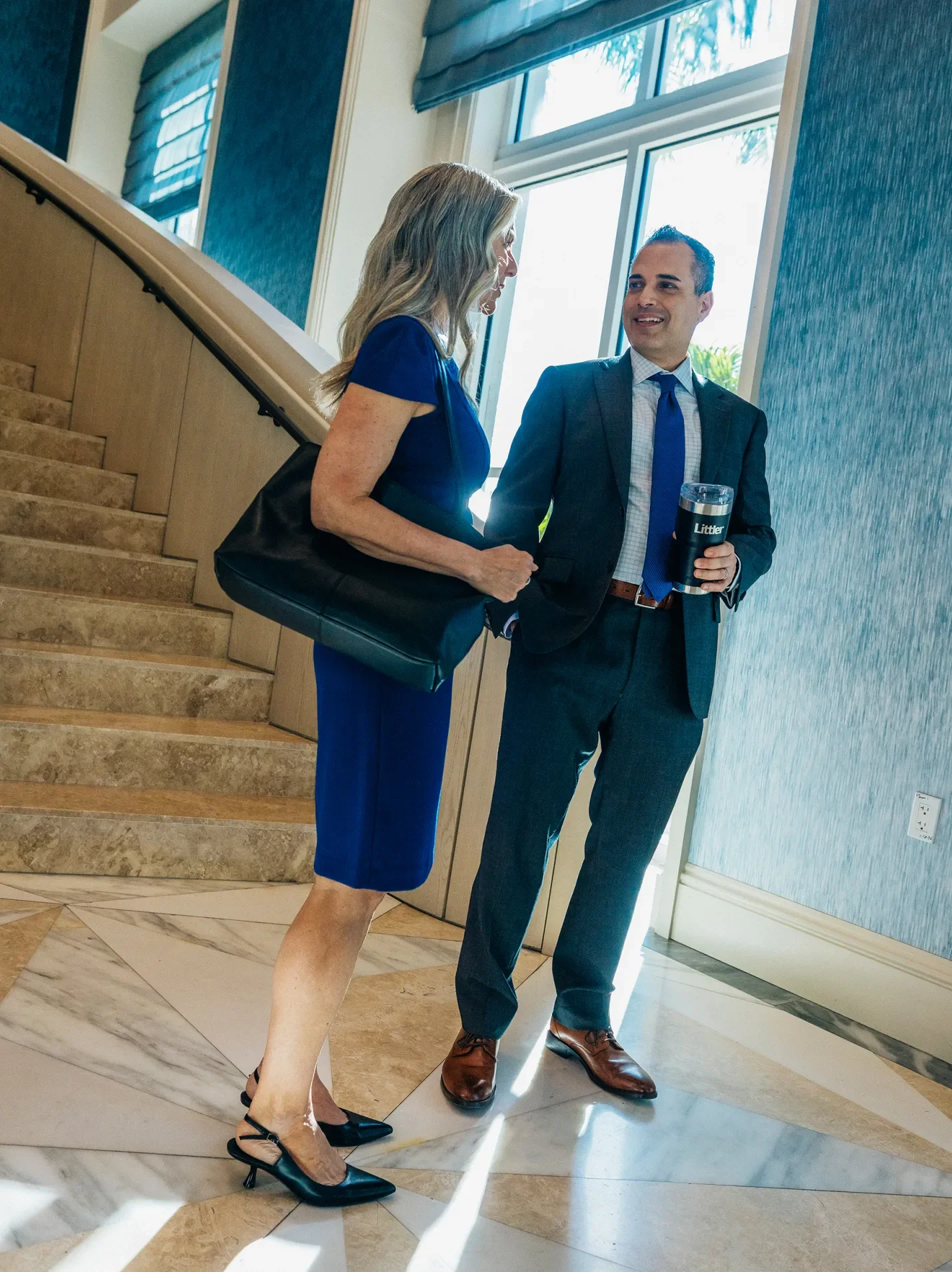 Woman and man in business attire talking near a staircase in an office building