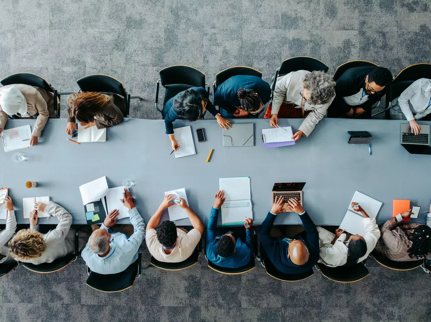 Overhead view of large conference table with people seated along both sides meeting