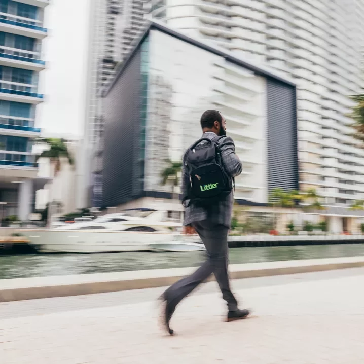 A man in a suit carrying a Littler backpack walks along a city street with a blurred background