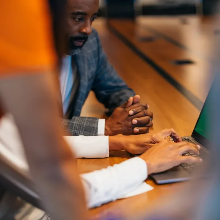 Man sitting at a table next to a woman using a laptop computer