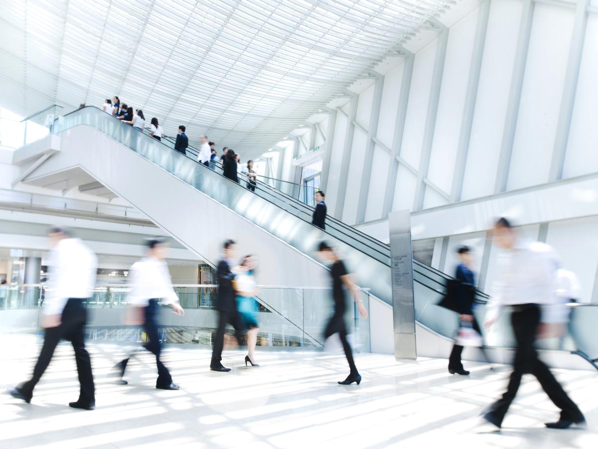 Blurred people walking in an office building lobby with a staircase in the background