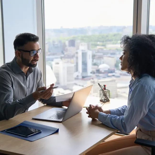 Man and woman interviewing across a desk with a laptop